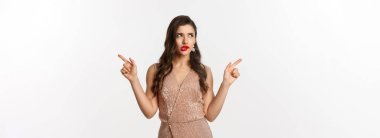 Noel partisi. Cazibeli düşünceli kadın parmaklarını yana doğru gösteriyor, seçim yapıyor, düşünüyor, sağdan soldan teklifler sunuyor, beyaz arka planda duruyor..