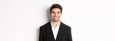 Yakından bakınca şık takım elbiseli yakışıklı genç iş adamı gülümsüyor, beyaz arka planda duruyor..