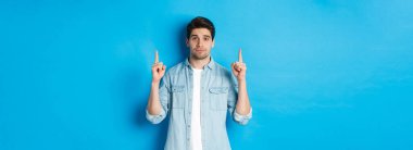 Sakin ve yakışıklı bir adamın size tanıtım teklifini göstermesi, fotokopi alanını göstermesi, mavi arka planda durması..