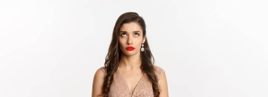 Hoşnutsuz, saç stili ve makyajlı, beyaz arka planda duran üst düzey reklamlara bakan genç bir kadının yakın çekimi..