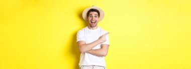 Turizm ve yaşam tarzı kavramı. Reklam veren mutlu genç erkek turist, solu işaret ediyor ve gülümsüyor heyecanlı, sarı arka plan.