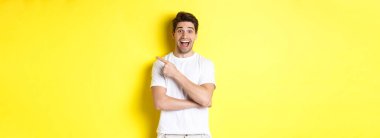 Heyecanlı gülümseyen bir adam resmi. Kara Cuma teklifleri sunuyor, parmağıyla işaret ediyor ve şaşırmış görünüyor. Sarı arka planda duruyor..