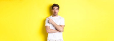 Şaşırmış yakışıklı adamın portresi sağ eli işaret ediyor, hayret içinde, sarı arka planda duruyor..