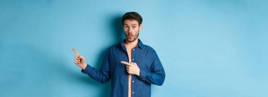 Şaşkın genç adam tanıtımı kontrol ediyor, parmaklarını logoya doğrultuyor ve 