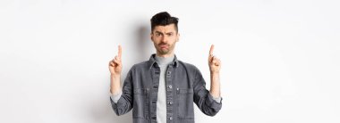 Kafası karışmış, bıyıklı, garip bir şeyi işaret eden, kaşlarını çatan, kafası karışmış, beyaz arka planda duran komik adam..