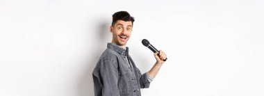 Mikrofon tutan yakışıklı bir adamın profili. Heyecanlı yüzüyle kameraya dön, karaoke yap ve stand-up yap, beyaz arka planda dur..