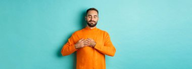 Yakışıklı adam nostaljik hissediyor, kalbi tutuyor ve hayal kuruyor, bir şeyleri hatırlıyor ya da hayal ediyor, turkuaz arka plana karşı kaygısız duruyor..