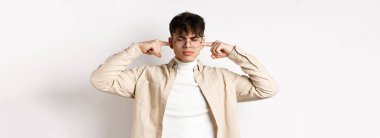 Sinirli genç adam kulaklarını kapattı, sinir bozucu sesi engelledi, dinlemek istemedi, beyaz arka planda durdu..