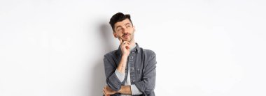 Düşünceli yakışıklı adam dalgın dalgın bakıyor, seçim yapıyor, beyaz arka planda duruyor..