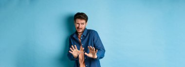 Adam siner ve çirkin şeylerden uzak durur, yana bakar ve kötü anlaşmayı reddetmek için ellerini uzatır, mavi arka planda durur..