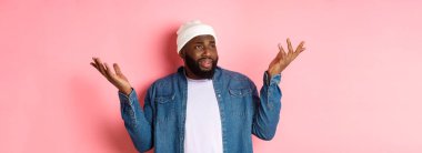 Şüpheci şaşkın adam saçma bir şeye bakıyor, sola bakıyor ve omuz silkiyor, kafası karışmış, pembe arka planda duruyor..