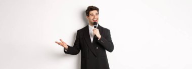 Siyah takım elbiseli yakışıklı bir adamın portresi şarkı söylüyor, mikrofon tutuyor ve konuşma yapıyor, beyaz arka planda duruyor..