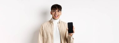Teknoloji ve online alışveriş konsepti. Gözlüklü neşeli yakışıklı adam boş akıllı telefon ekranı gösteriyor ve gülümsüyor, uygulamayı gösteriyor, beyaz arka planda duruyor..