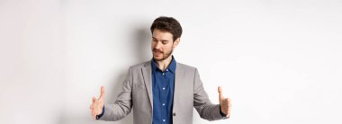 Heyecanlı yakışıklı iş adamı uzun boyda bir şey gösteriyor. Ellerini uzatıp beyaz arka planda duran büyük bir nesne..