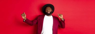 Noel ve insanlar kavramı. Mutlu siyah adam yeni yılı kutluyor ve dans ediyor, parti kıyafeti giyiyor, kırmızı arka plan.