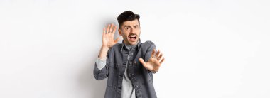 Korkmuş ürkek adam çığlık atıyor ve ellerini kaldırıyor. Durmak için yalvarıyor, saldırıdan korunuyor, beyaz arka planda duruyor..