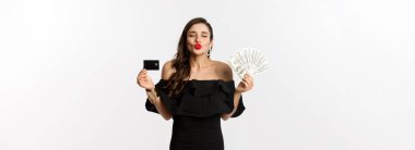 Güzellik ve alışveriş konsepti. Güzel, çekici bir kadın öpüşmek için dudaklarını büzüyor, kredi kartı ve dolar gösteriyor, beyaz arka planda duruyor..