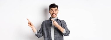 Bana bak. Mutlu stil sahibi bir adam gülümsüyor, parmaklarını boşluğa doğrultuyor, havalı tanıtım teklifleri sunuyor, beyaz arka planda kot ceket giyiyor..