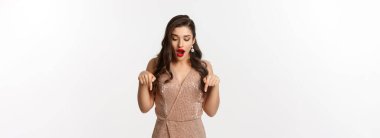 Parti elbisesi içinde şaşaalı bir kız. Şaşkın şaşkın bakıyor ve işaret ediyor. Yılbaşı ilanı gösteriyor..