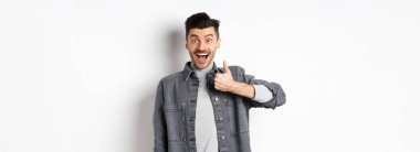 Aferin, çok iyi. Heyecanlı yakışıklı adam güzel işi övüyor, parmağını kaldırıyor ve gülümsüyor mutlu, harika seçimi onaylıyor, beyaz arka planda duruyor..