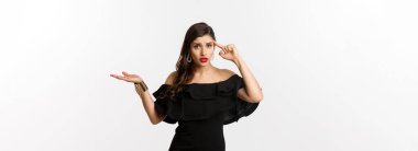 Moda ve güzellik. Sinirli ve rahatsız bir kadın kafasını işaret ediyor, aptalca bir hata yüzünden birini azarlıyor, kafası karışmış görünüyor, beyaz arka planda duruyor..