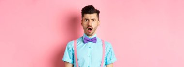 Şok olmuş ve gücenmiş genç bir adam pembe arka planda aşağılanmış, kaba birine bakıyor..