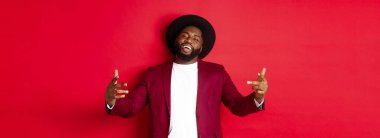 Noel alışverişi ve insanların konsepti. Kendine güvenen ve küstah bir adam jestle dans ediyor, hip hop yapıyor ve kamera karşısında kendinden emin, kırmızı arka planda..