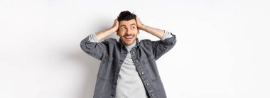 Heyecanlı genç adam rahatlamış ve mutlu görünüyor, gülümsüyor ve logoya bakıyor, el ele tutuşuyor neşeli, beyaz arka planda duruyor..