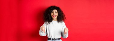 Heyecanlı kadın parmaklarını aşağıya doğru gösteriyor ve şaşkın bir şekilde gülümsüyor, şuraya bakın, kırmızı boşlukta logo gösteriyor..