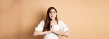 Umut dolu genç kız Tanrı 'ya yalvarıyor ve sol üst köşede rüya gibi görünüyor, dua ediyor ya da dilek tutuyor, bej arka planda duruyor..