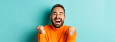 Tatmin olmuş yakışıklı bir adamın görüntüsü, kazanmanın sevinci ya da başarının sevinci, yumruk tokuşturmak ve evet demek, turkuaz arka planda durmak..