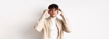 Gözlüklü, baş ağrısı çeken, baş şakaklarına dokunan, migrenden kaşlarını çatan, başı dönen, beyaz arka planda duran genç bir adamın görüntüsü..