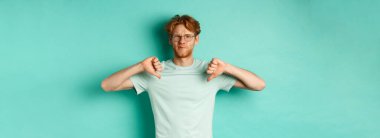 Kırmızılı, dağınık saçlı, gözlüklü, bir şeyi beğenmeyen, üzgün ve hoşnutsuz, daracık arkaplan başında duran, hayal kırıklığına uğramış beyaz adam..