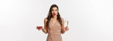 Parti ve kutlama konsepti. Kırmızı dudaklı, çekici elbiseli, şampanya içen, pasta yiyen, kameraya şaşırmış zarif bir kadın..