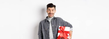 Sevgililer günün kutlu olsun. Şaşkın ve mutlu bir adam elinde hediye kutusuyla kameraya bakıyor, şaşırmış bir şekilde gülümsüyor, bayramı kutluyor, romantik bir randevuya hediyesini getiriyor, beyaz bir geçmişi var..