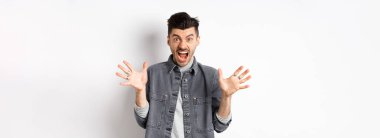 Kızgın adam çığlık atıyor ve kameraya bakıyor, öfkeli ve nefret dolu bir ifadeyle bağırıyor, beyaz arka planda duruyor..