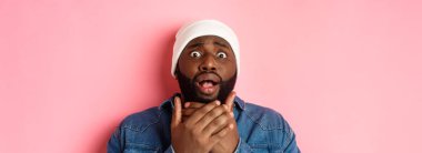 Şok olmuş ve korkmuş Afrikalı-Amerikalı adam kameraya bakıyor, endişeli, pembe arka planda duruyor..