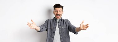 Heyecanlı genç adam kucaklaşmak için ellerini uzat, sana sarıl, misafirleri karşıla ve gülümse, insanları davet et, beyaz arka planda dur..