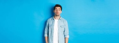 Yakışıklı bir adam öpüşmeyi bekliyor, dudaklarını büzüyor, gözlerini kapatıyor ve mavi arka planda duruyor..