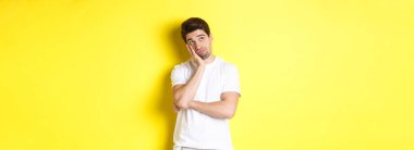 Sıkılmış ve kasvetli adam yukarı bakıyor, bir şeyler hayal ediyor, sarı arka planda duruyor..