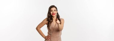 Cazibeli, parlak elbiseli zarif bir kadın seni işaret ediyor Noel tatili ve parti konsepti beyaz arka planda duruyor..