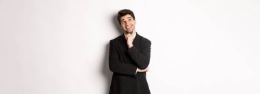 Şık bir parti elbisesi içindeki düşünceli gülümseyen adamın portresi, sol üst köşeye bakıyor ve düşünüyor, bir şeyler hayal ediyor, beyaz arka planda duruyor..