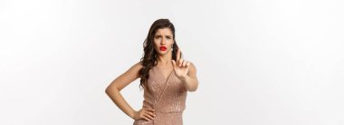 Kutlama, tatil ve parti kavramı. Cazibeli elbiseli, hoşnutsuz bir kadın parmaklarını sallıyor, onaylamıyor, bir şeyi yasaklıyor, hayır diyor, beyaz arka plan diyor..