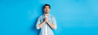 Çaresiz bir adam yardım için yalvarıyor, Tanrı 'ya yalvarıyor, el ele tutuşup dua ediyor, mavi arka plana karşı duruyor..