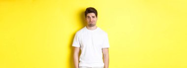 Üzgün, somurtkan ve somurtkan görünen, sarı arka plandan memnun olmayan bir adam..