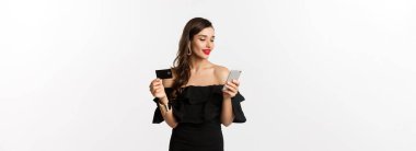 Moda ve alışveriş konsepti. İnternetten alışveriş yapan genç ve çekici bir kadın. Kredi kartı ve akıllı telefonuyla internet alıyor. Beyaz bir geçmişi var..