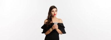 Akıllı telefon kullanan, düşünen, yukarı bakıp düşünen, beyaz arka planda duran düşünceli genç bir kadın. Boşluğu kopyala