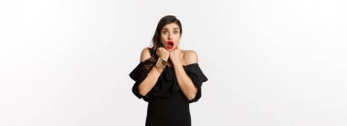 Çekici kadının portresi korkmuş ve şok olmuş bir şekilde kameraya bakıyor, korku dolu bir şeye bakıyor, siyah elbisenin içinde beyaz arka plana karşı duruyor..