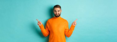 Şüpheli ve kararsız bir adam parmaklarını yana doğru uzatıyor, farklı tarafları gösteriyor, iki seçenek, şüpheci görünüyor, açık mavi arka planda duruyor..