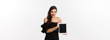 İnternetten alışveriş konsepti. Siyah elbiseli çekici bir kadın beyaz arka planda duran dijital tablet ekranı gösteriyor. Boşluğu kopyala
